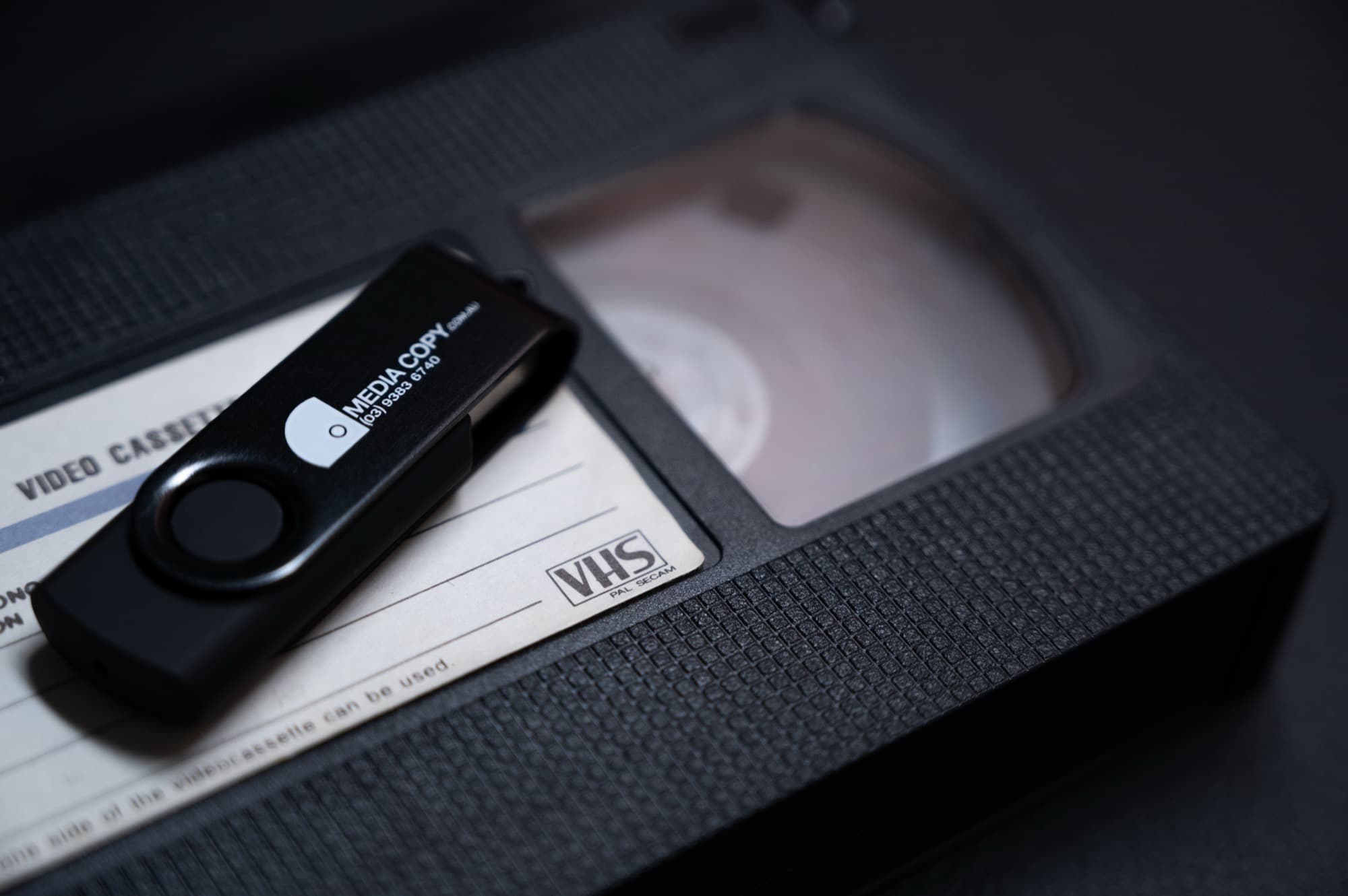 A branded Media Copy USB stick resting on a VHS tape